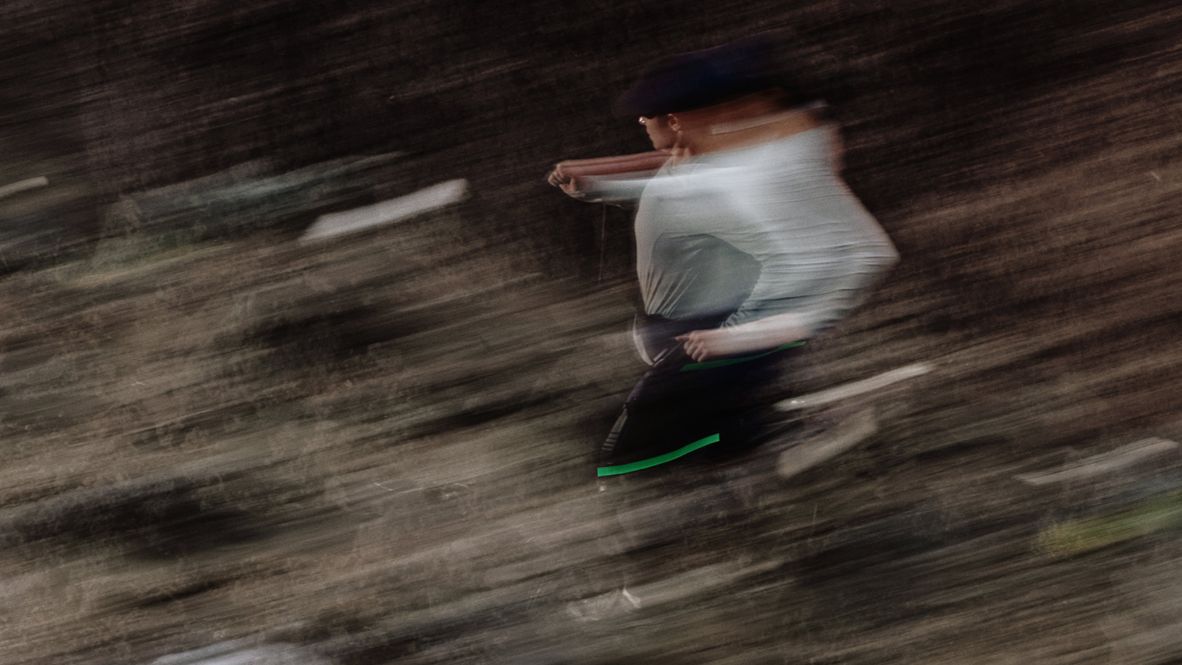 A person in a white top and dark skirt or pants captured in motion with strong horizontal motion blur against a dark brown textured background.